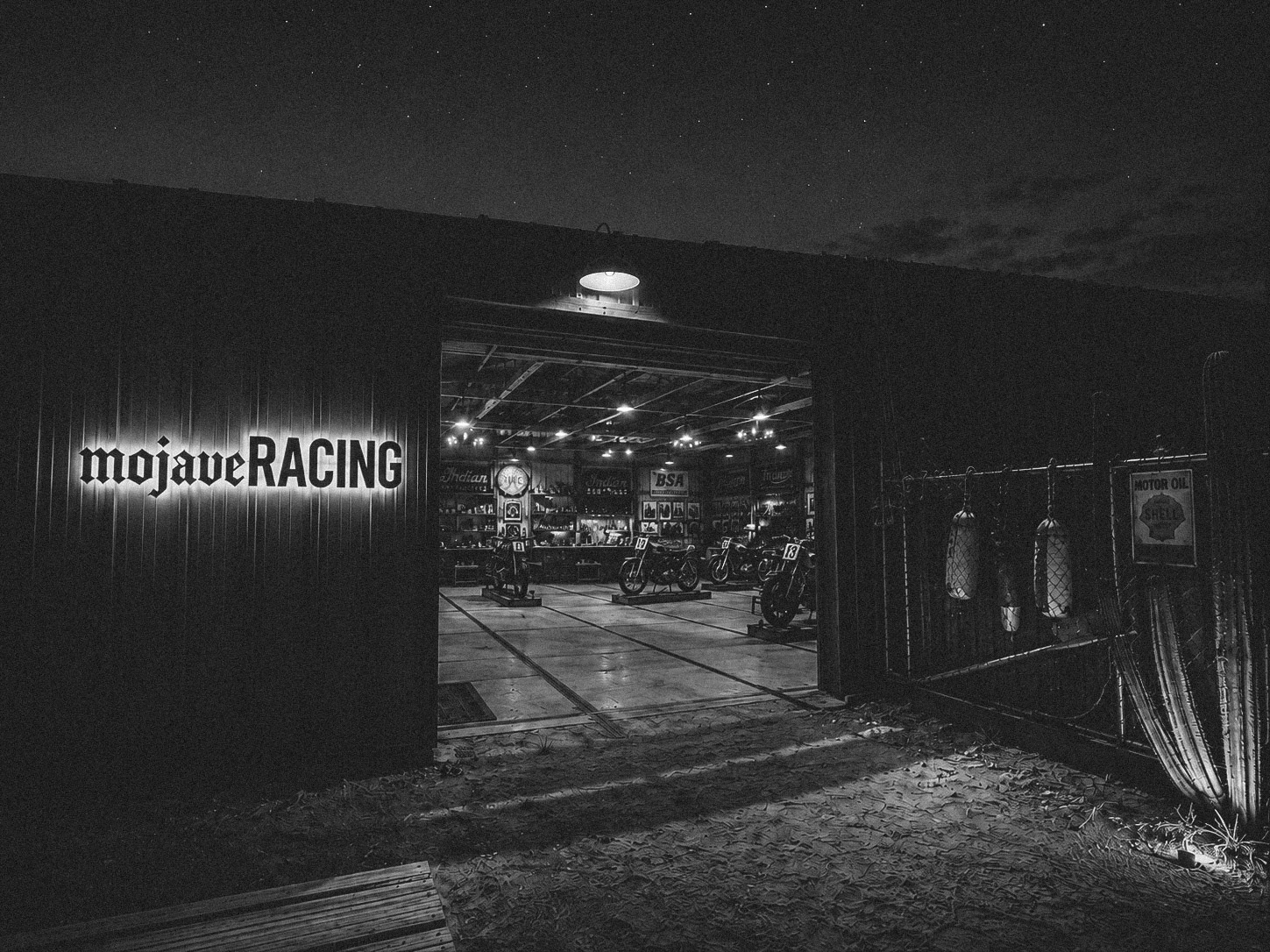 The illuminated Mojave Racing workshop filled with vintage motorcycles at night.