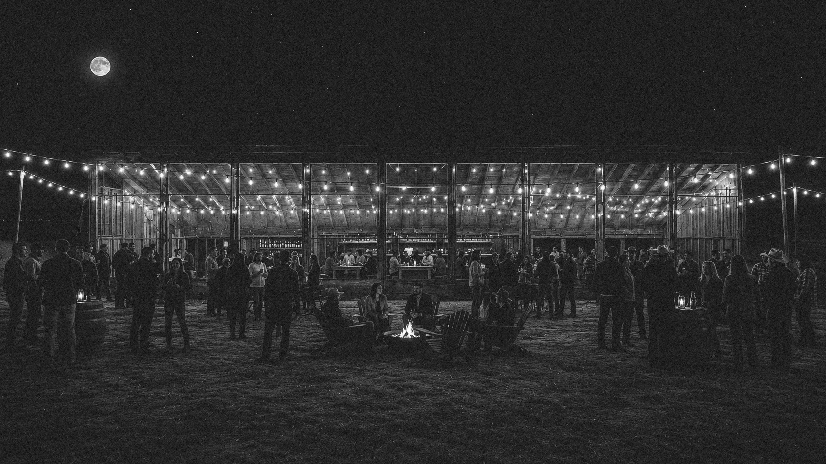 Friends gathered around a campfire outside the illuminated Mojave Ranch building.