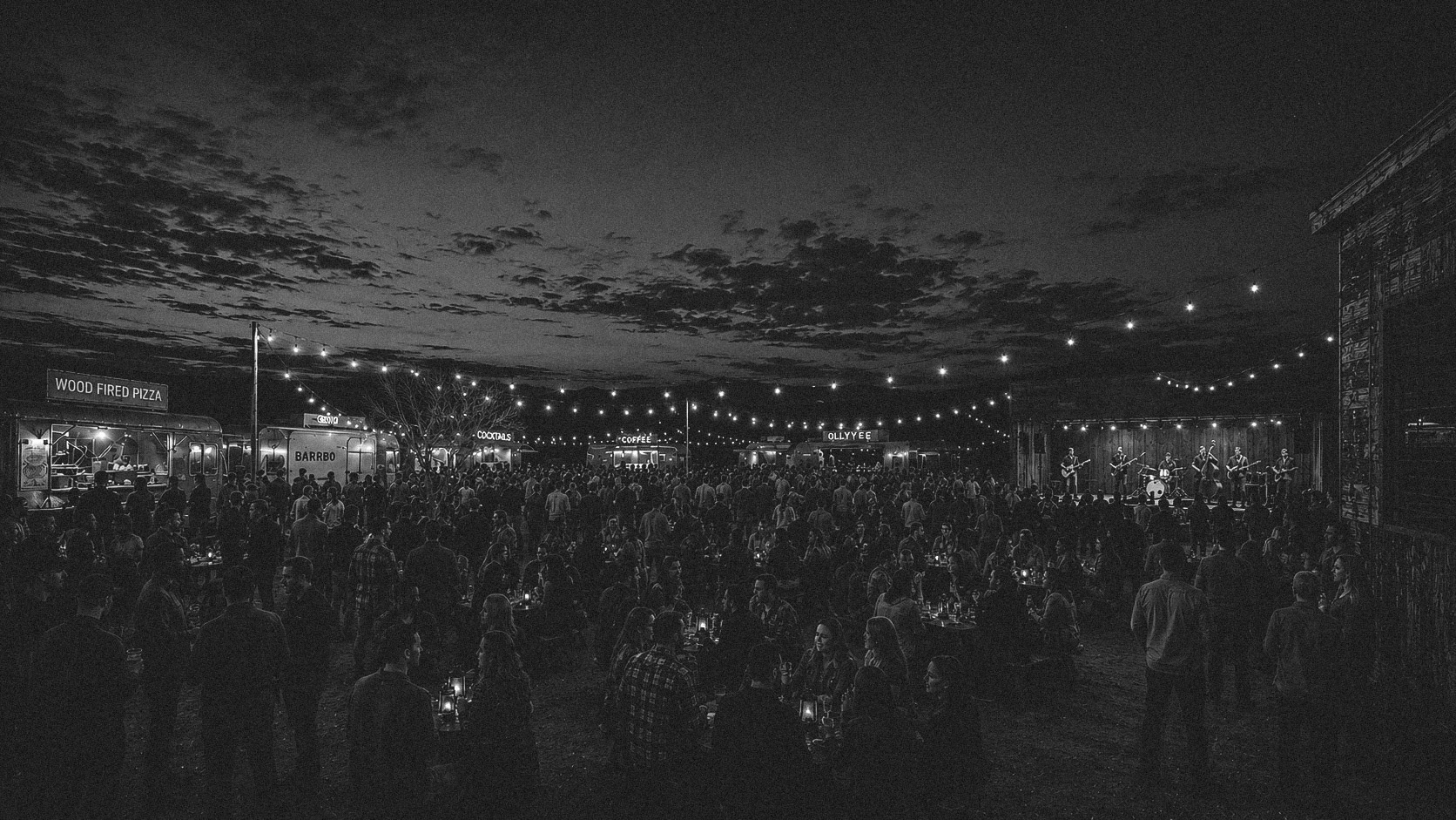 A festival crowd enjoying live music and food vendors beneath strings of lights.