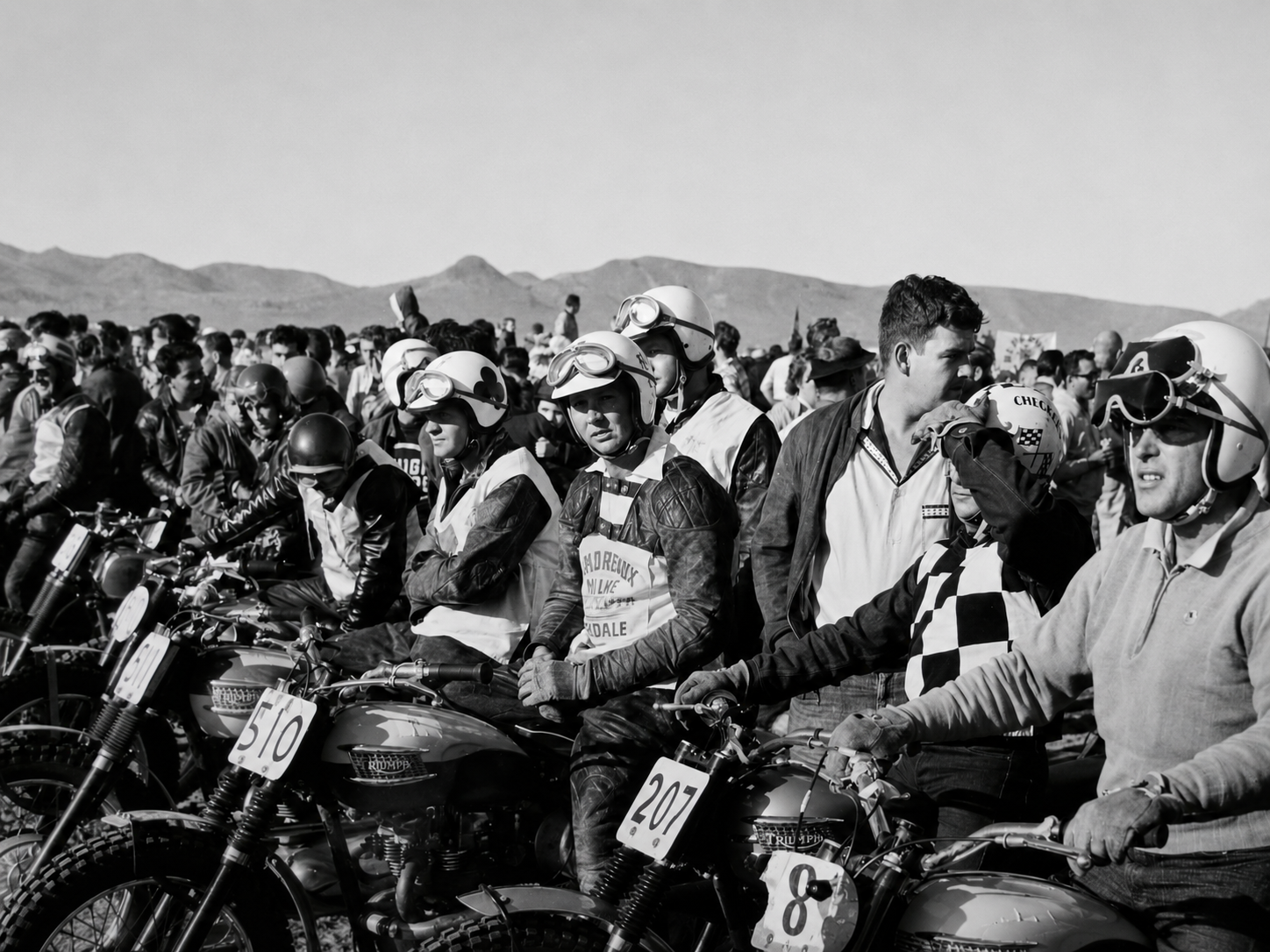 Vintage motorcycle racers lined up together in the desert.
