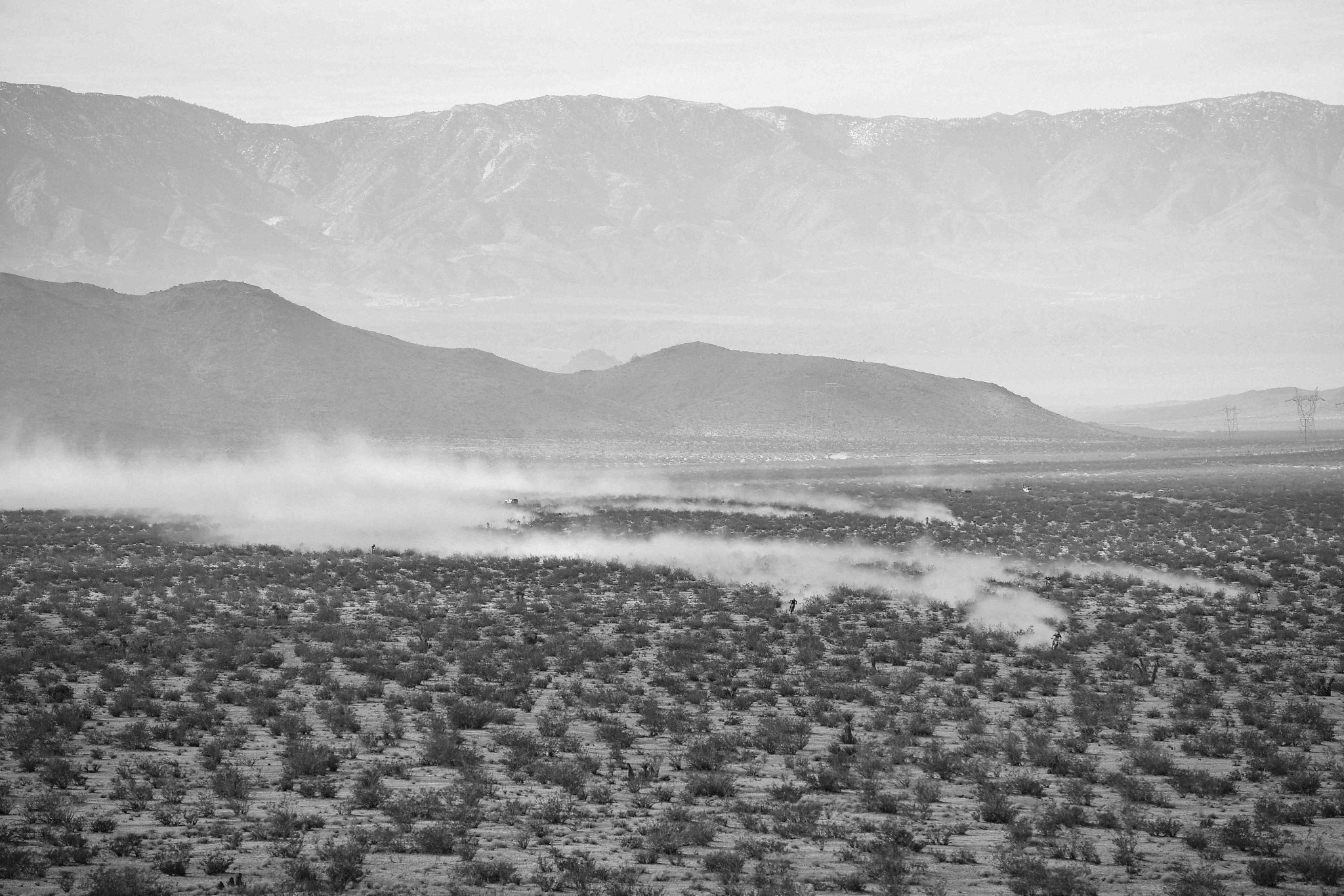 Racers leaving trails of dust across the desert beneath a mountain range.