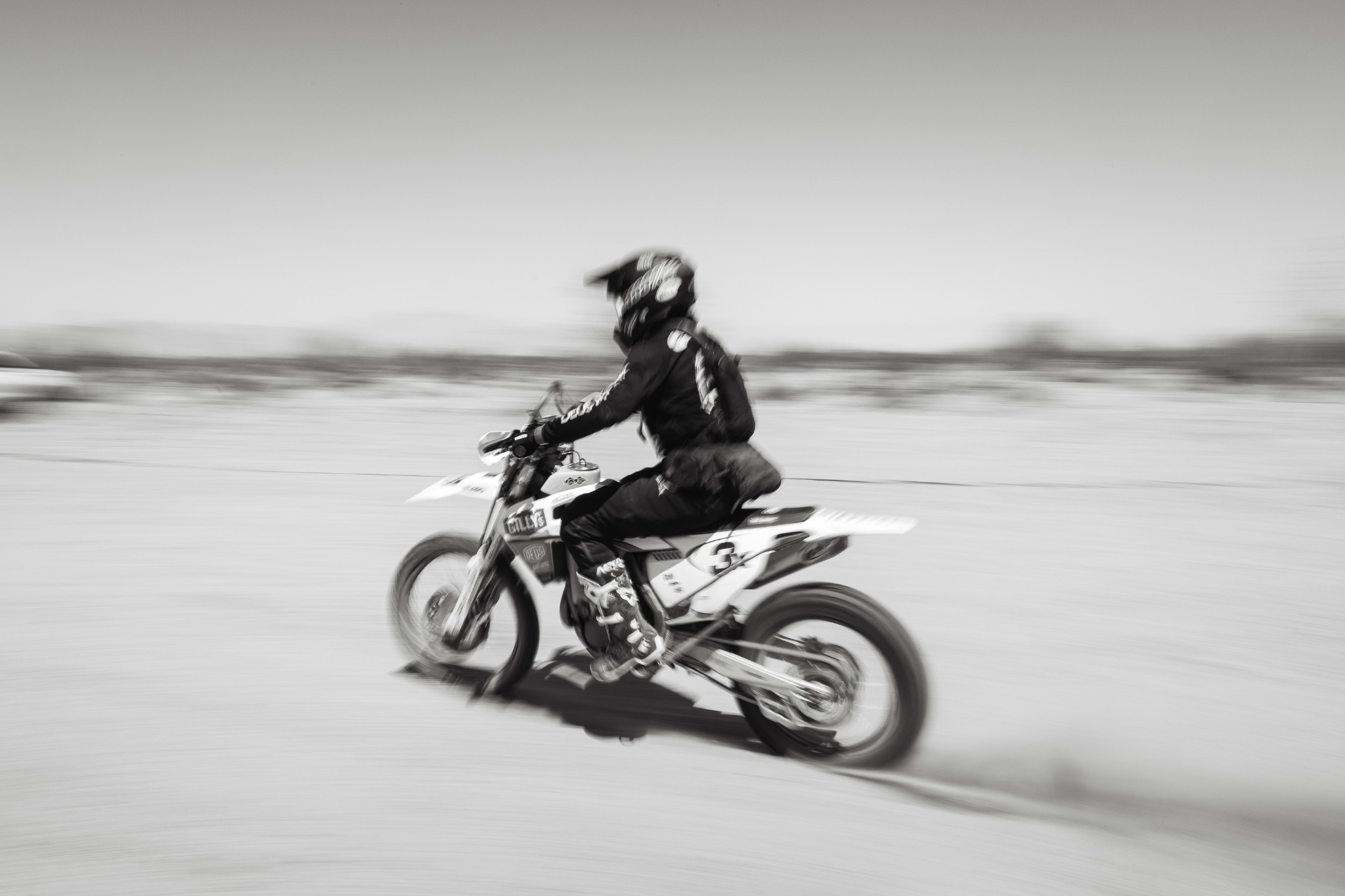A motorcycle racer moving across the desert in a motion-blurred action photograph.